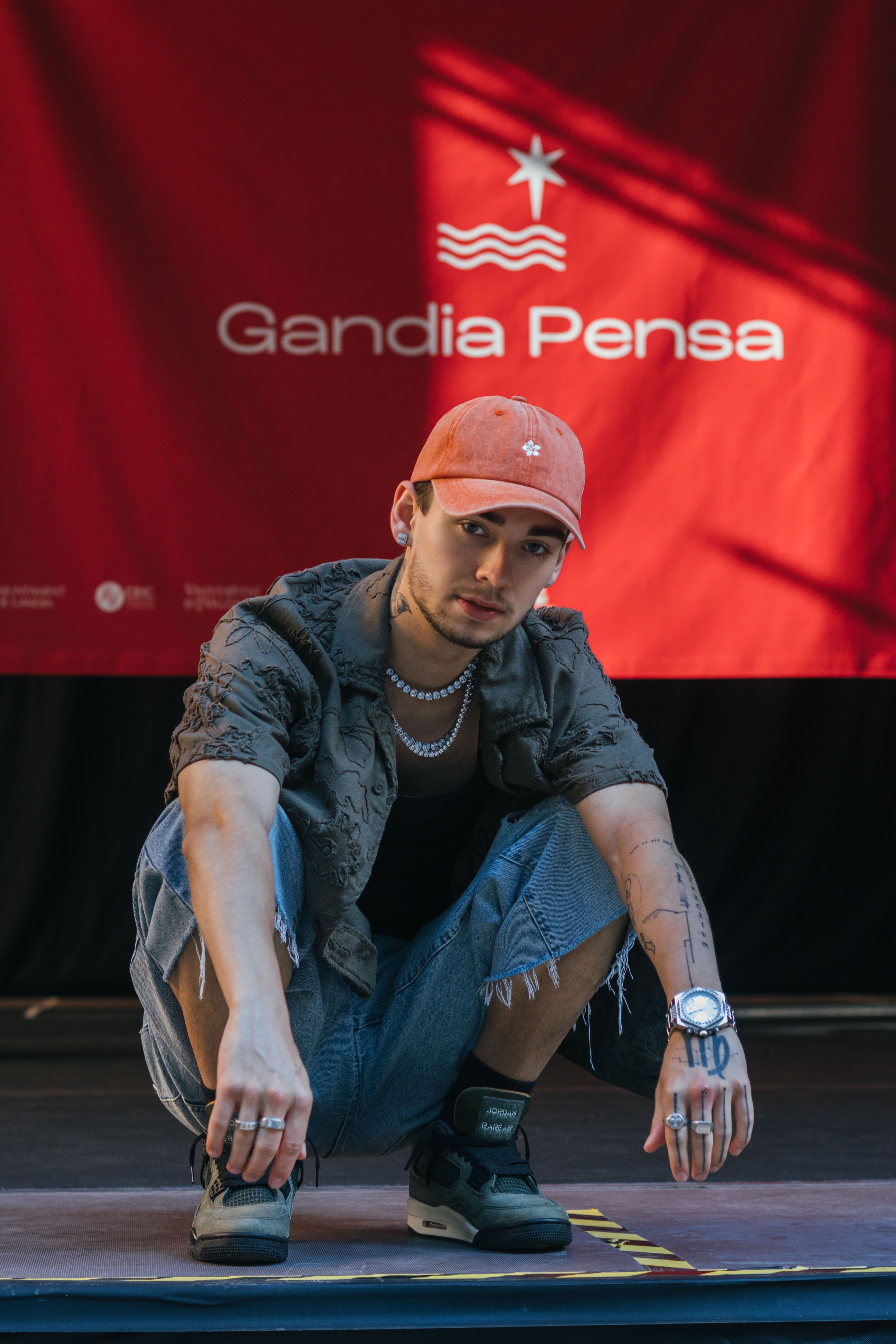 Stylish young man squatting in front of a red backdrop at Gandia Pensa event.