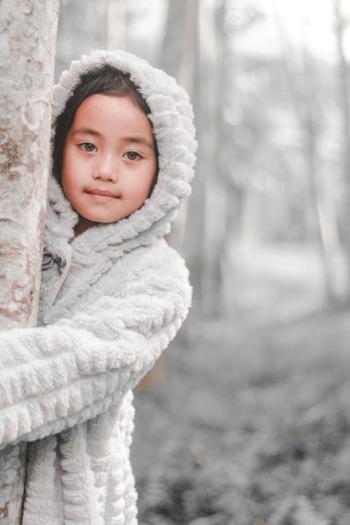 Girl Wearing Snow Jacket While Hugging Tree Trunk