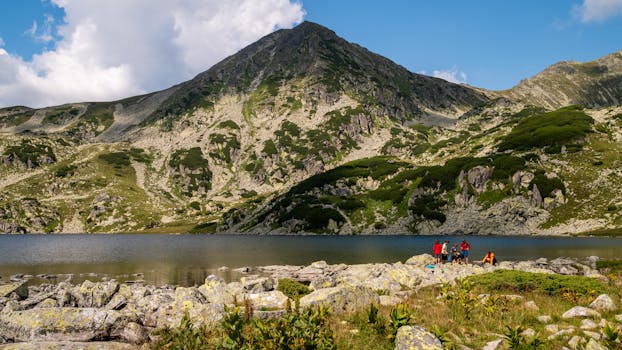A picturesque mountain landscape in Romania with hikers by a serene lake under a clear sky.