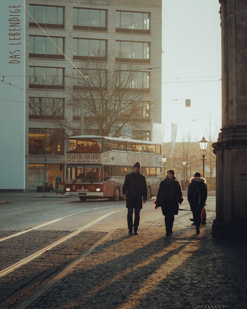 Free City streets at sunset with pedestrians and a bus casting long shadows. Stock Photo