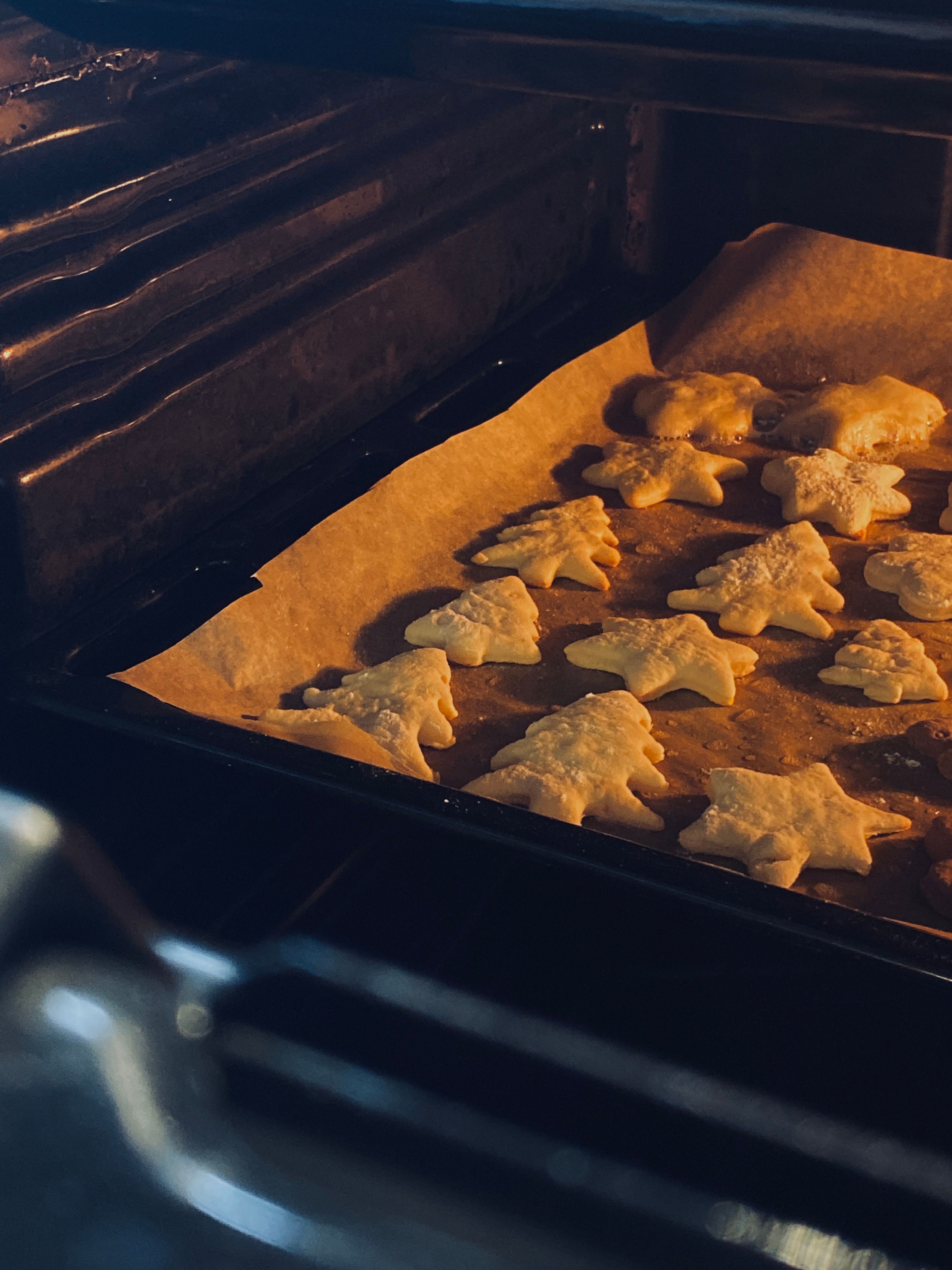 Festive star and tree-shaped cookies baking in an oven, captured with warm lighting.