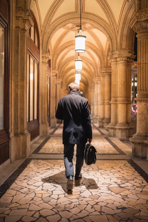 Free A solitary man walks through the illuminated arches of Vienna, showcasing classic architecture at night. Stock Photo