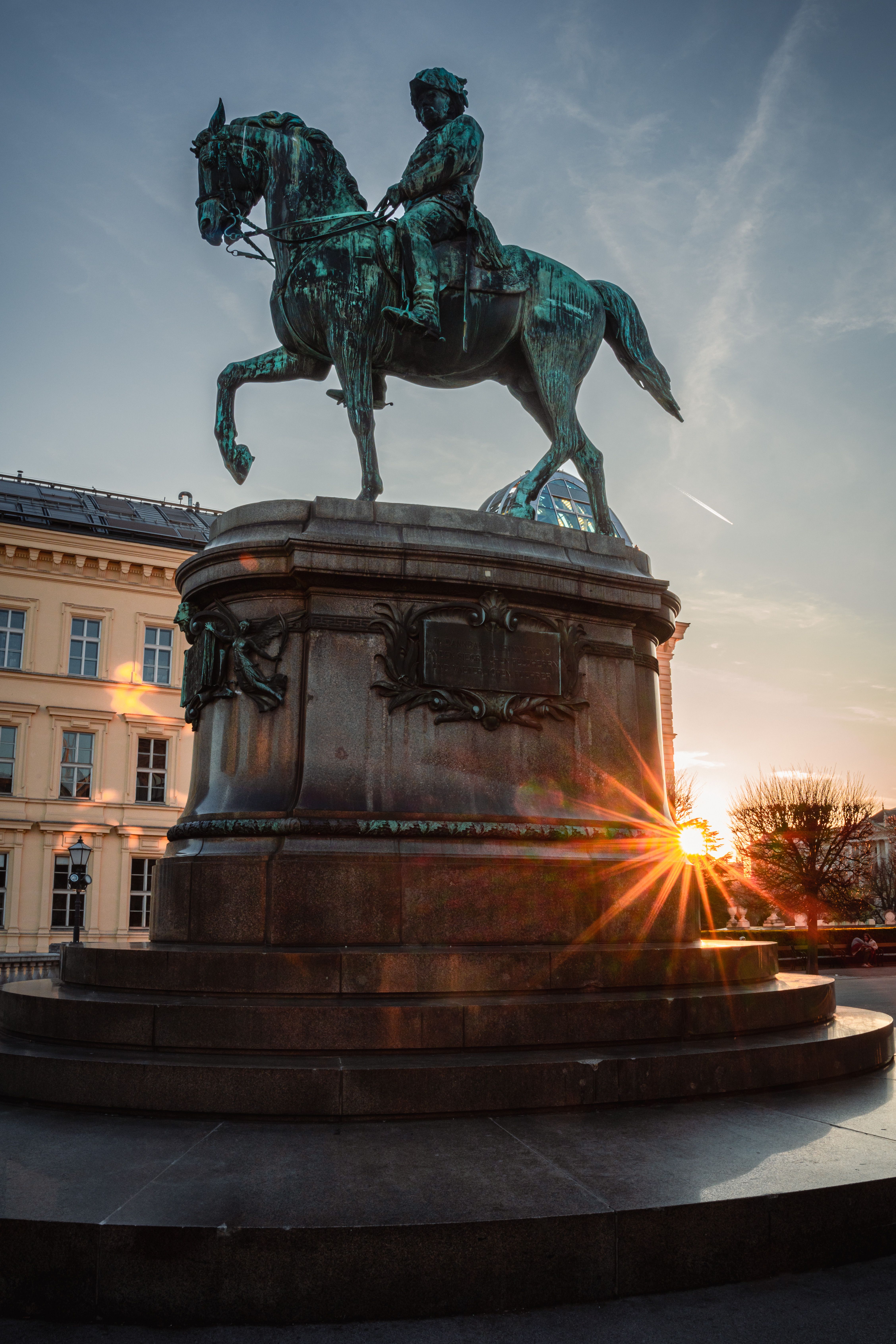 A majestic equestrian statue in Vienna captured beautifully at sunset with a dramatic sunburst effect.