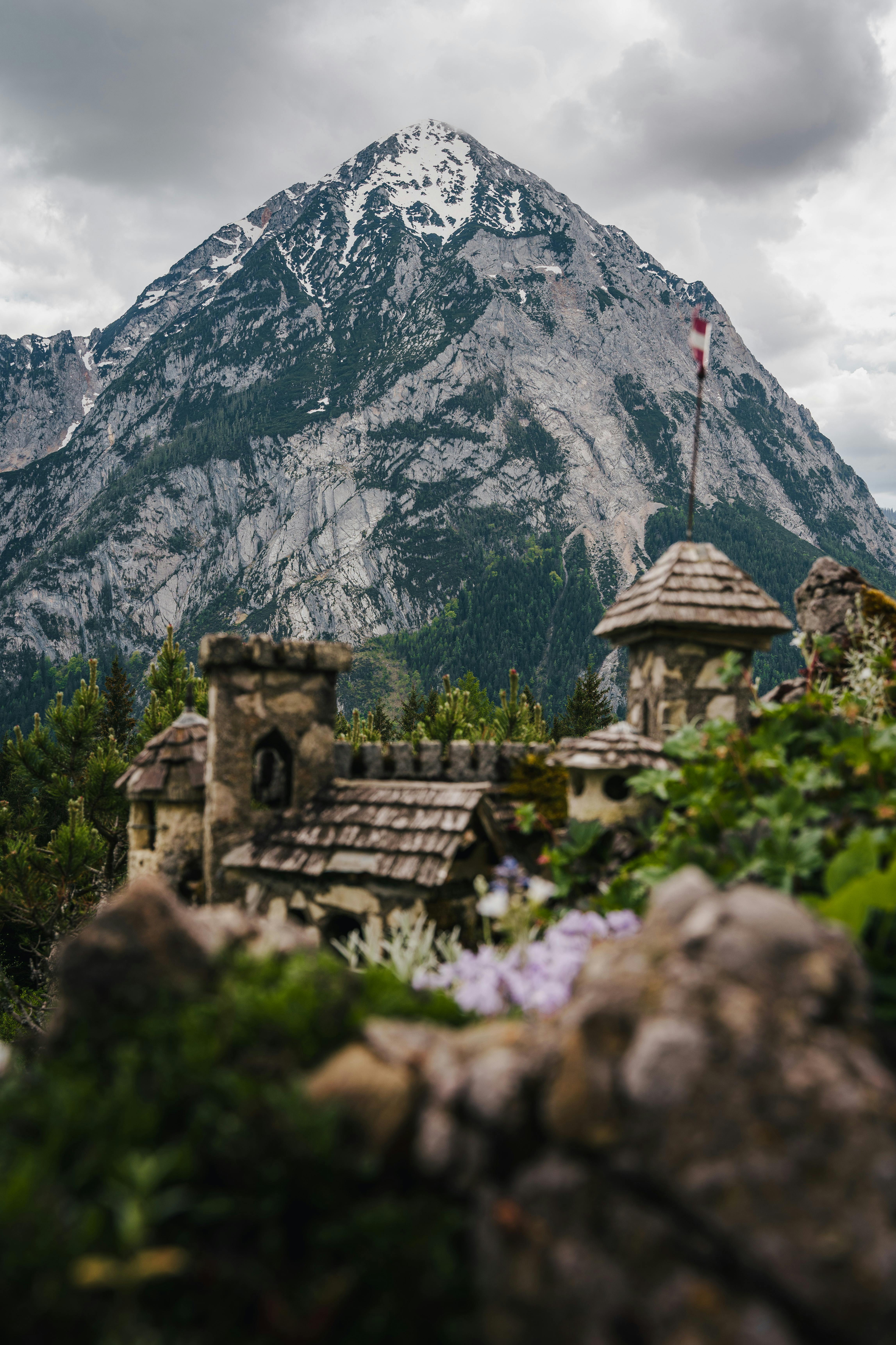 Gratis Primo piano di un castello rustico con imponenti montagne sullo sfondo sotto un cielo nuvoloso. Foto a disposizione