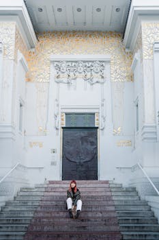 Young woman sits on steps of Vienna's Secession Building, highlighting its architectural grandeur.