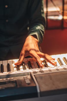 A close-up view of a person playing an electronic keyboard with warm sunlight casting shadows.