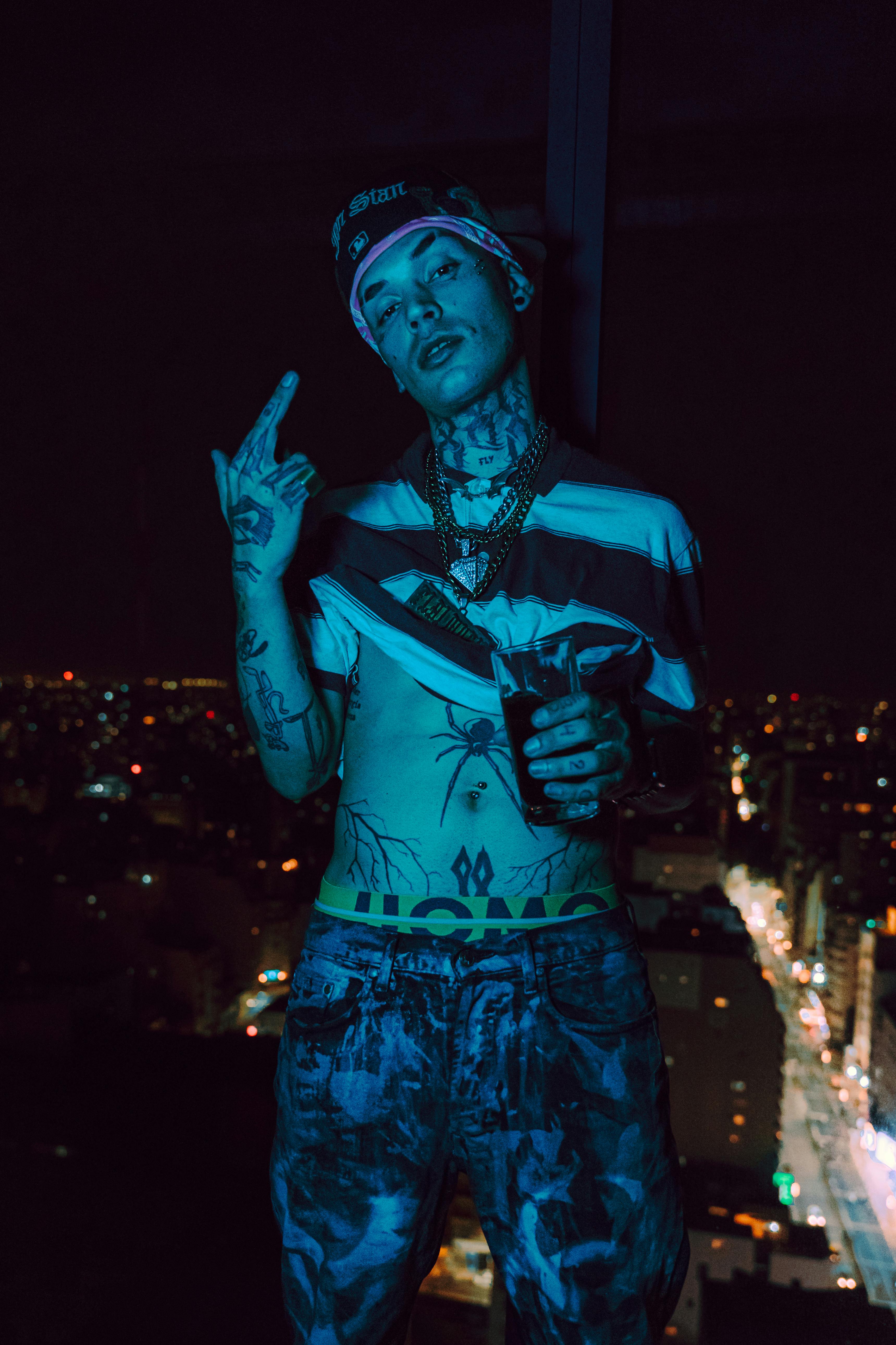 Tattooed person poses confidently against nighttime city skyline, expressive and bold.