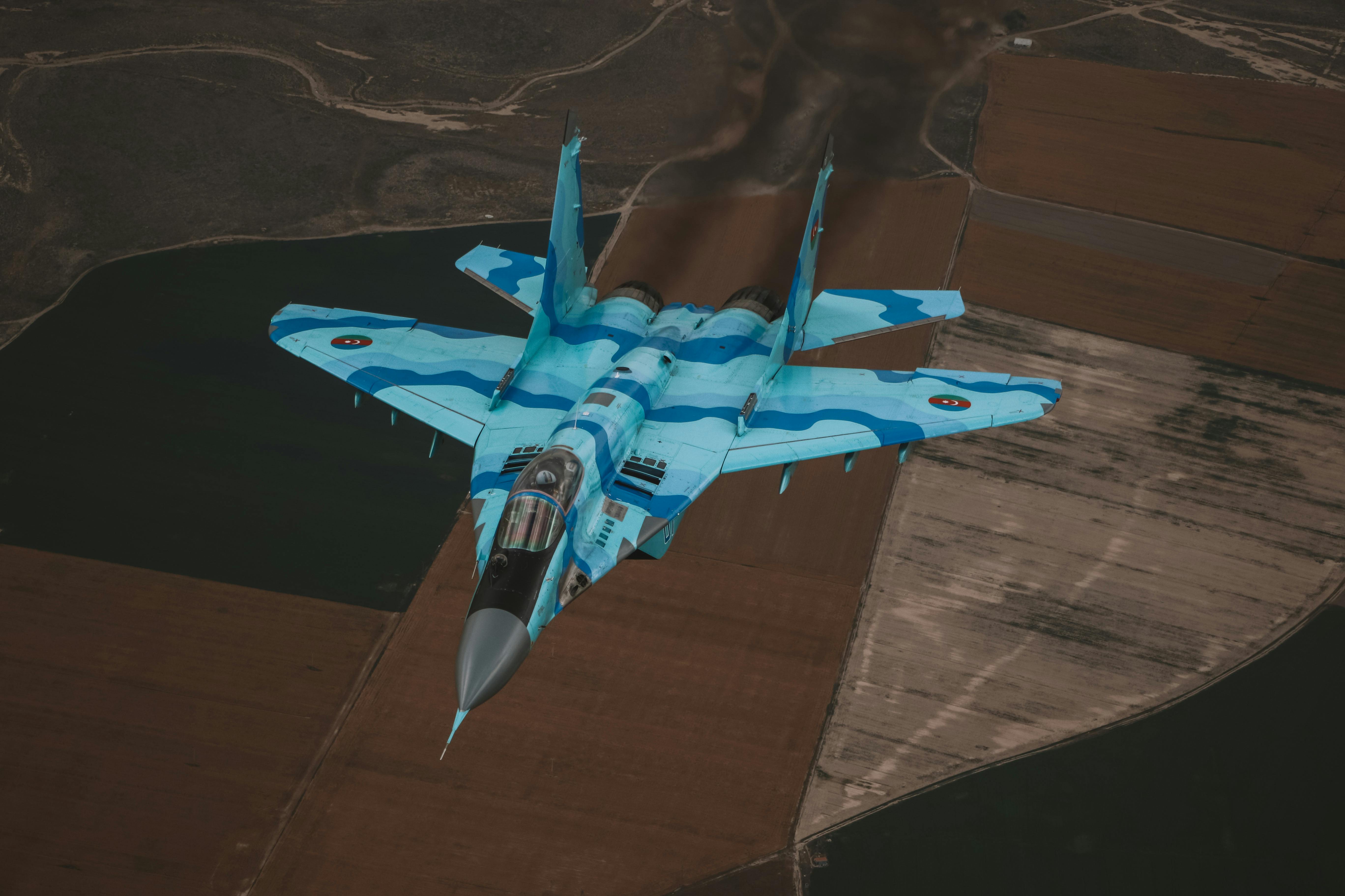 High-angle shot of a combat military jet flying over rural fields displaying speed and agility.