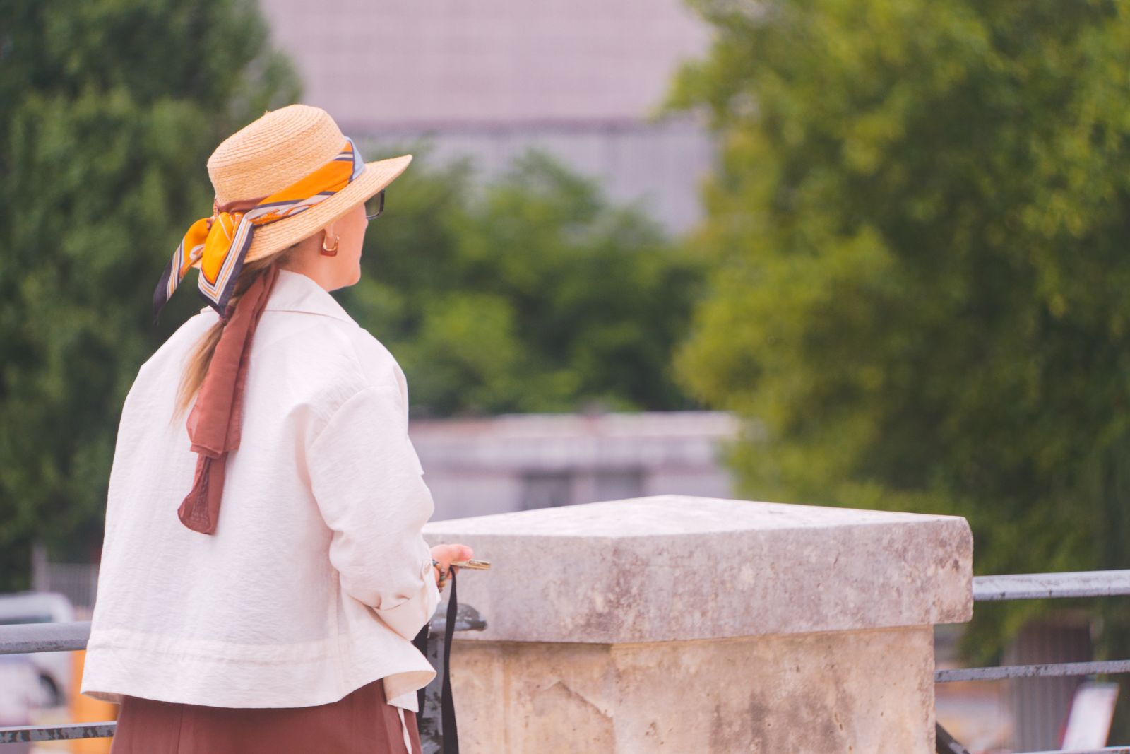 Femme au chapeau de paille et foulard appuyée sur un parapet de pierre
