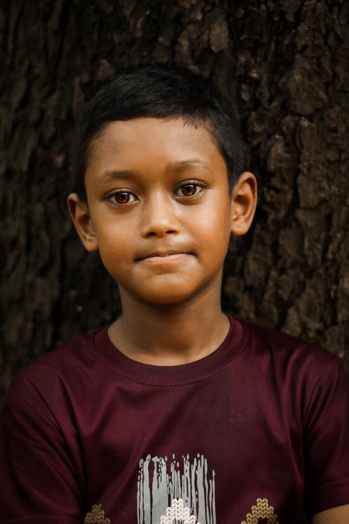 Free Close-up portrait of a young boy standing against a tree in Dhaka, Bangladesh. Stock Photo