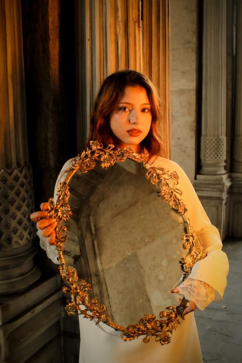 Free A woman in a white dress holding an ornate mirror in dramatic indoor lighting. Stock Photo