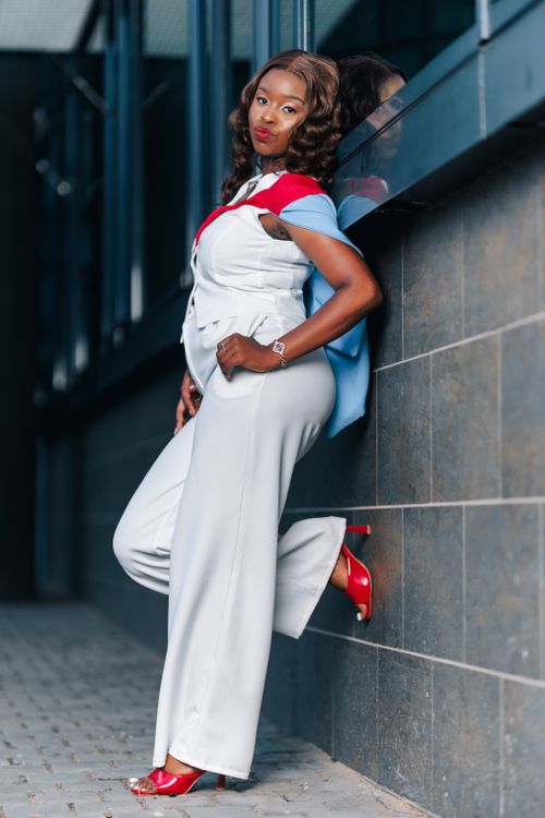 Free Elegant model in a white jumpsuit with red accents posing confidently against an urban wall. Stock Photo