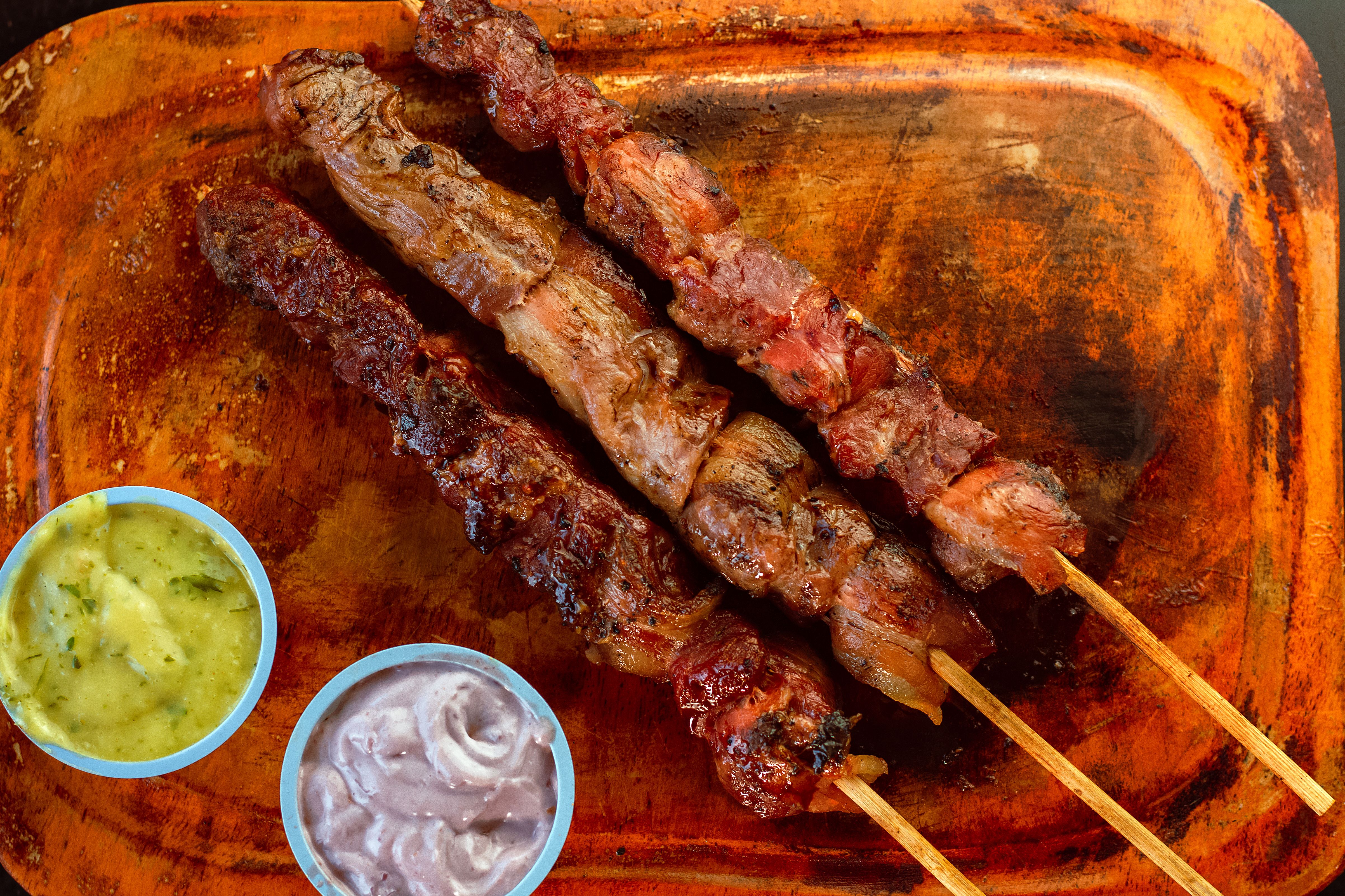 Delicious grilled meat skewers served with green and purple sauces on a rustic wooden board.