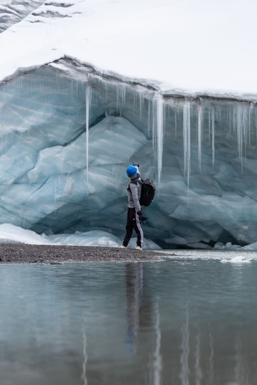 Free Person with helmet exploring an icy glacier cave. Reflective water foreground adds depth. Stock Photo