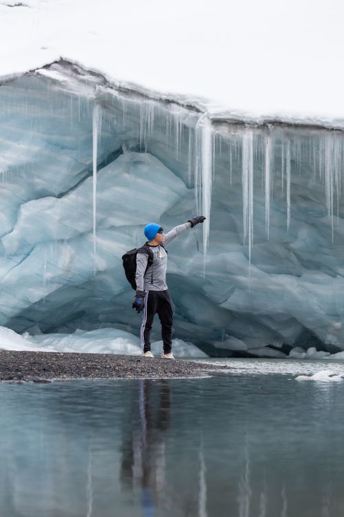 Free Man in activewear explores icy cave with hanging icicles, winter adventure. Stock Photo