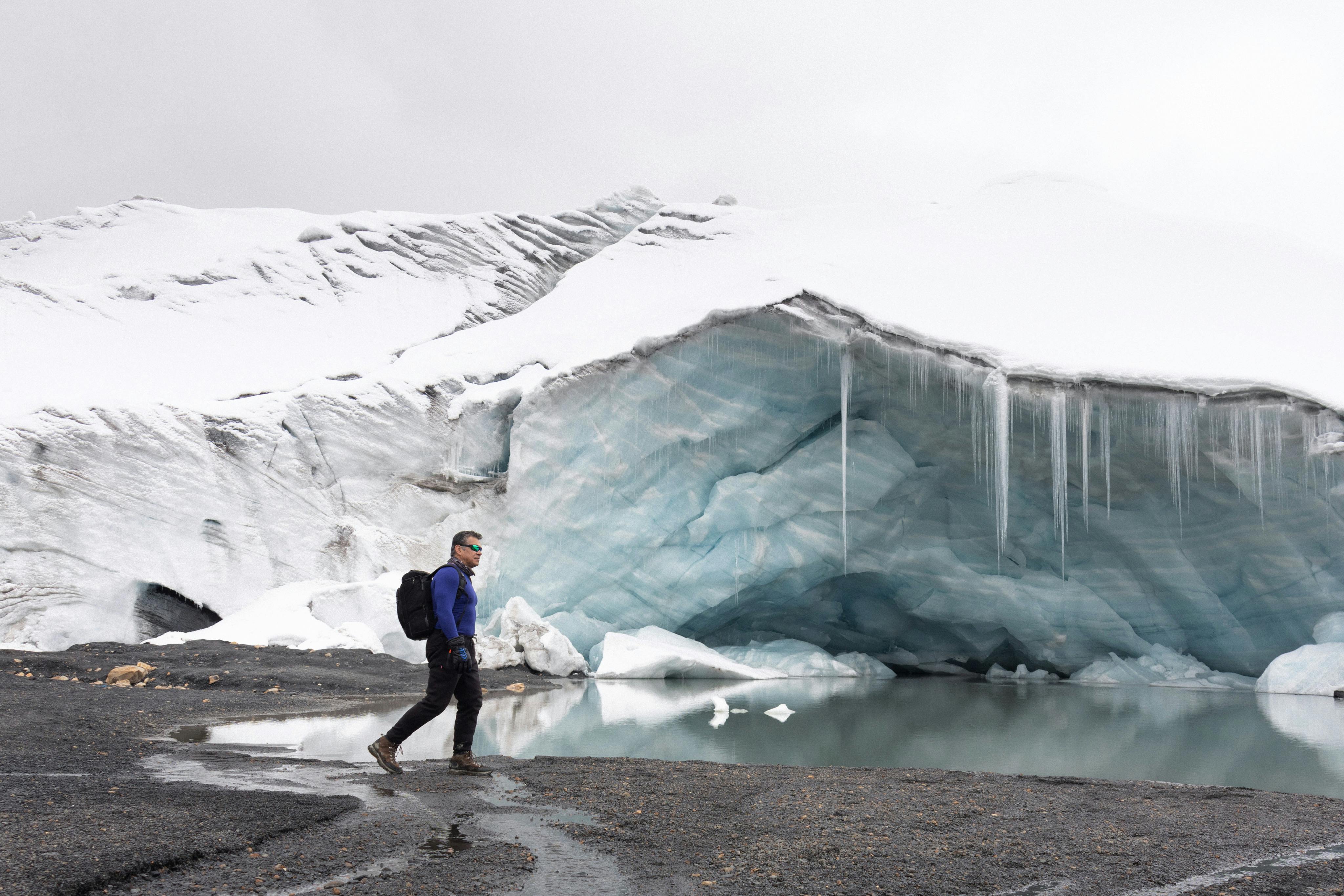 徒步旅行者在冰雪碧绿的冰洞附近探索，捕捉到冬日宁静的景象