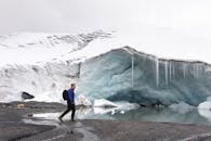 徒步旅行者在冰雪碧绿的冰洞附近探索，捕捉到冬日宁静的景象