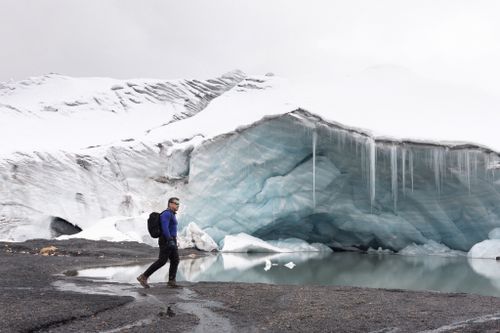 Free Hiker explores near ice cave with turquoise ice and snow, capturing a tranquil winter scene. Stock Photo