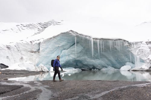 Free A person exploring the icy terrain beside a serene ice cave and reflective water. Stock Photo
