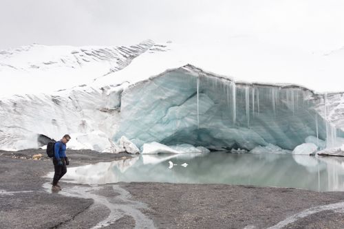 Free A lone traveler walks near a stunning glacial ice formation reflecting in calm water. Stock Photo