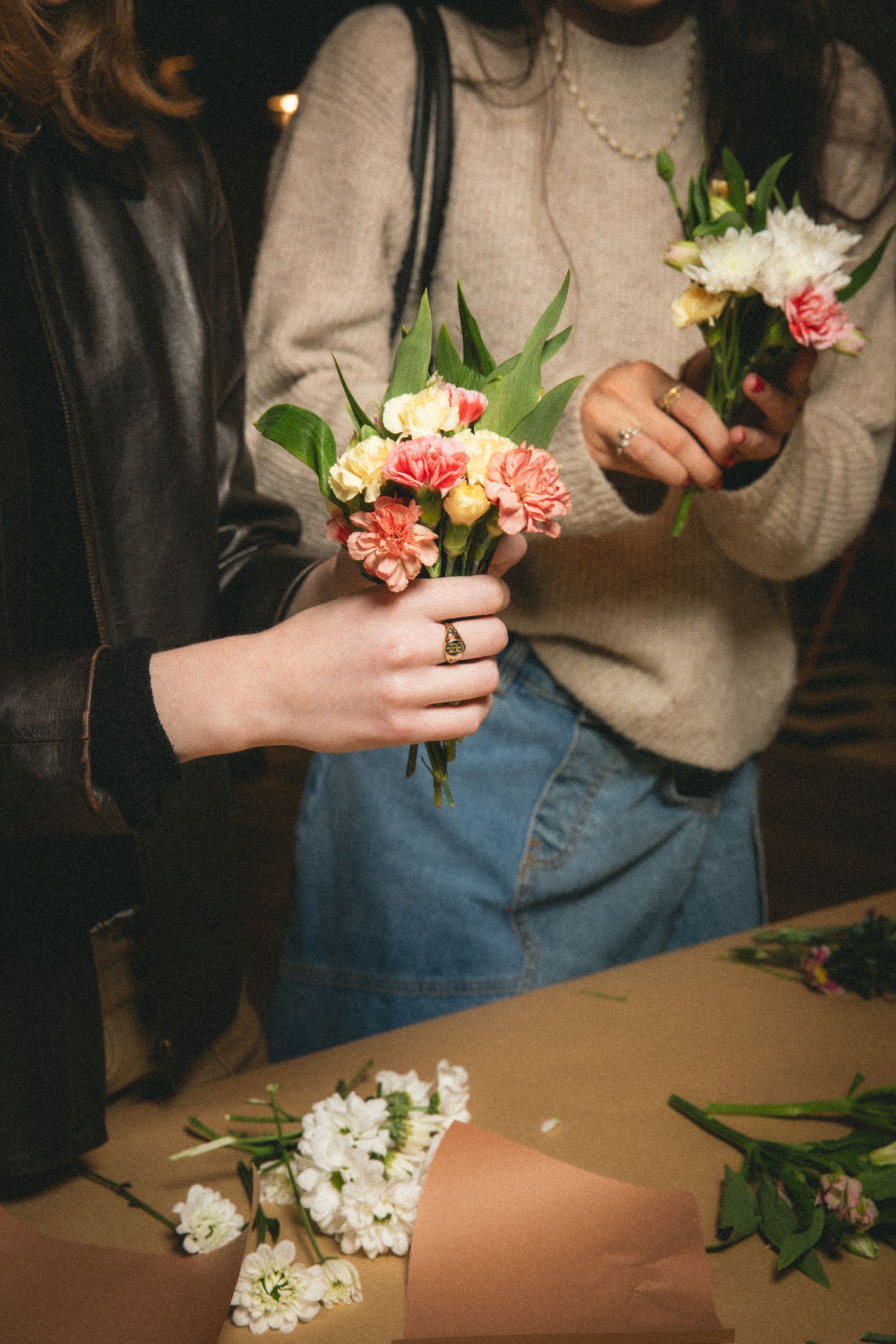 Two women arranging flower bouquets together at a workshop table.