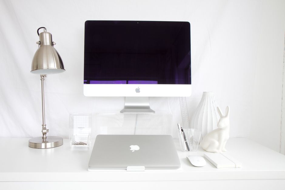 A sleek and tidy white desk setup featuring a desktop computer, lamp, and decorative items.