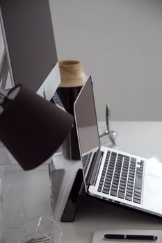 Minimalist office setup featuring a laptop, desktop, and modern lamp on a white desk.