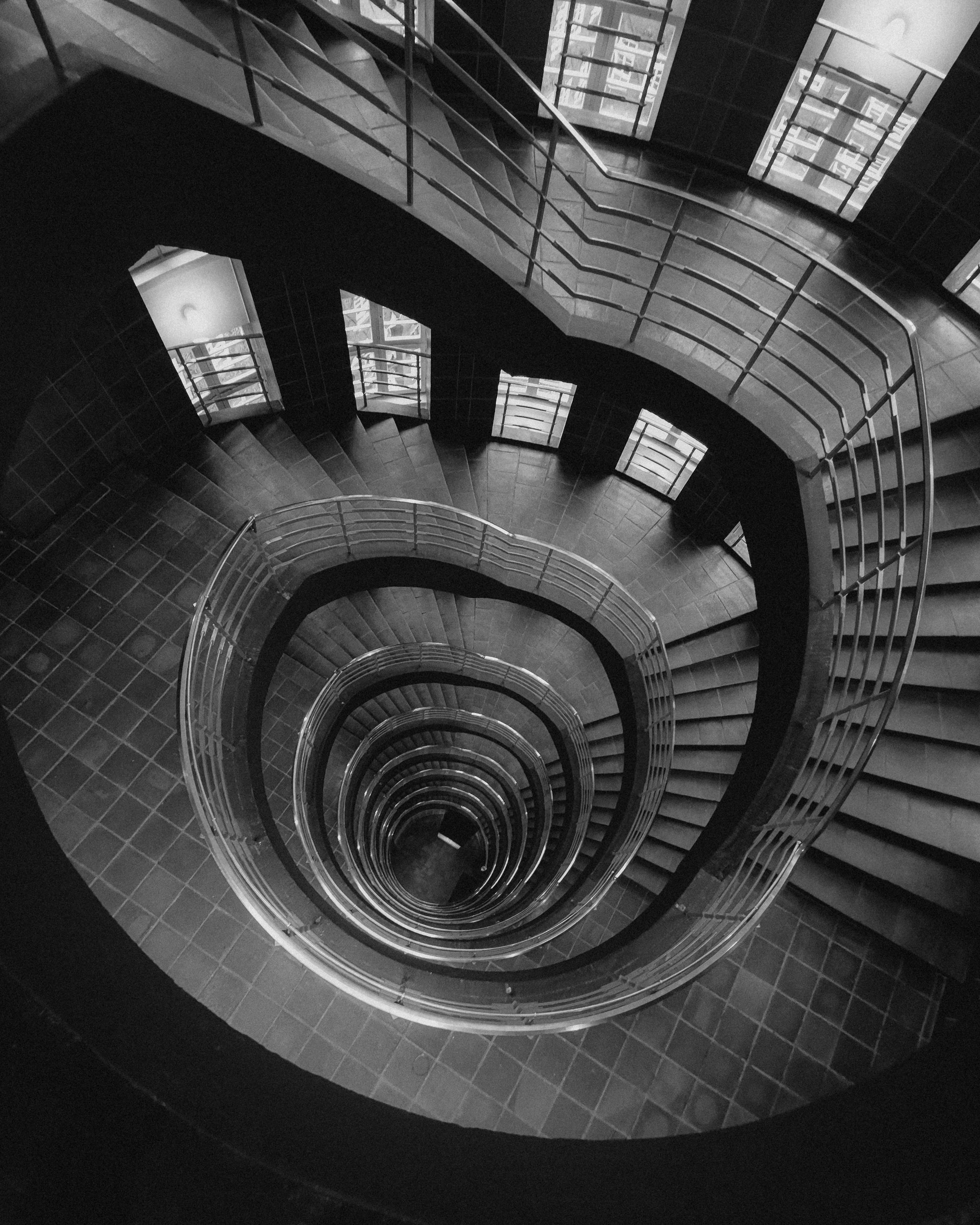 Dramatic black and white photo of a spiral staircase viewed from above.