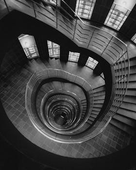 Dramatic black and white photo of a spiral staircase viewed from above.
