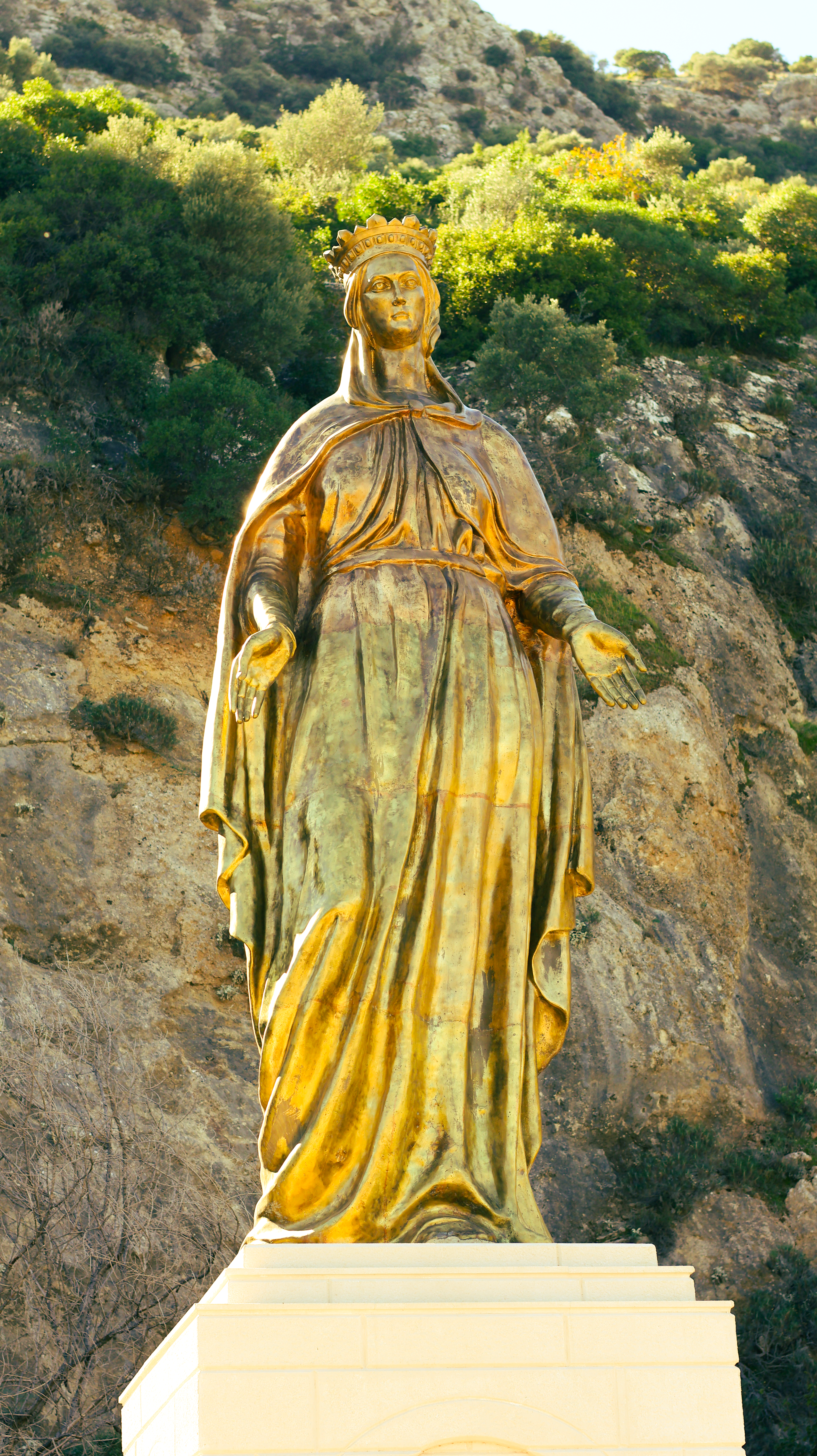 Majestic golden statue of a woman in flowing robes with rocky mountain backdrop.