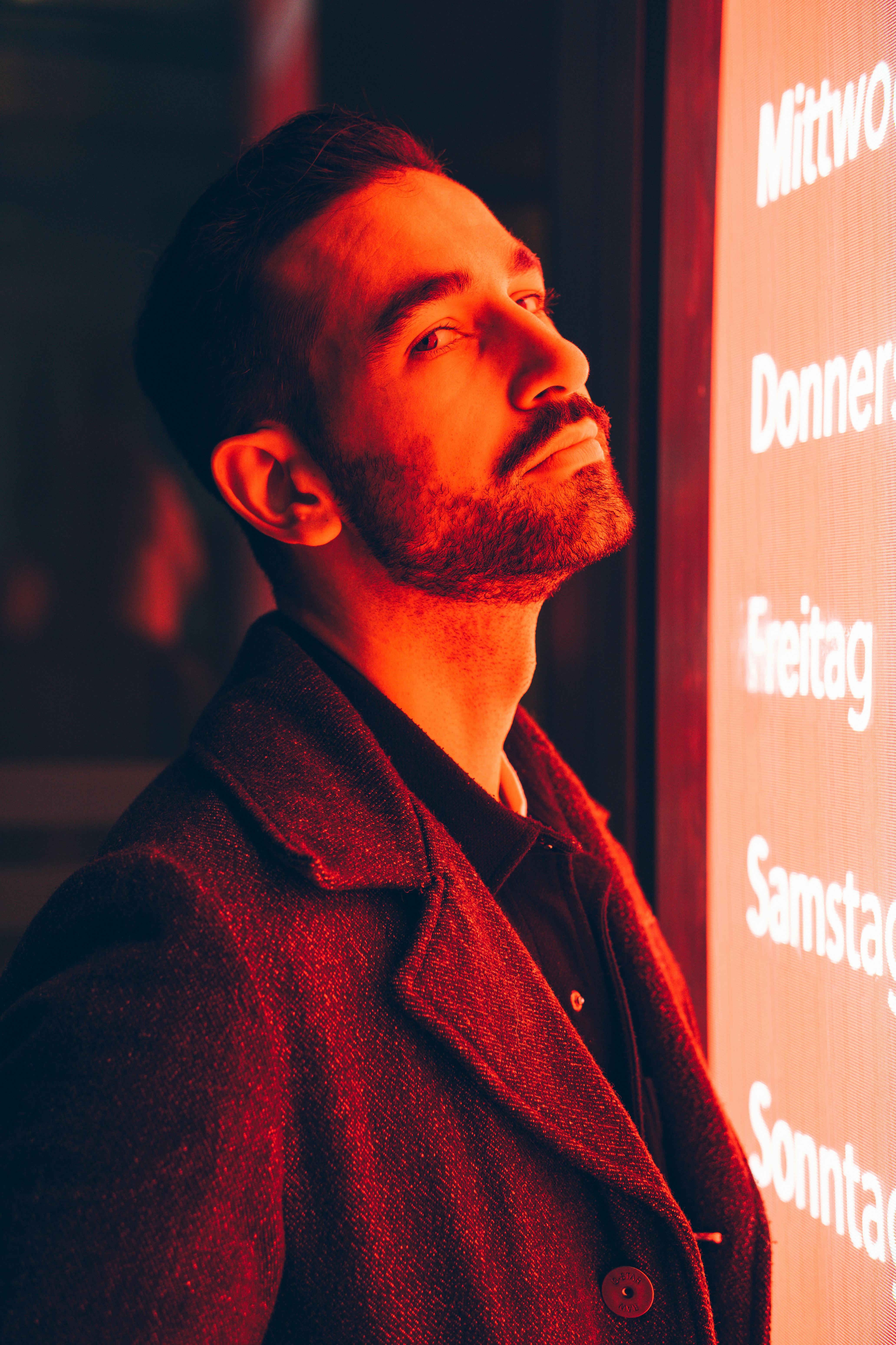 Stylish man's portrait illuminated by red neon light, creating a dramatic effect.