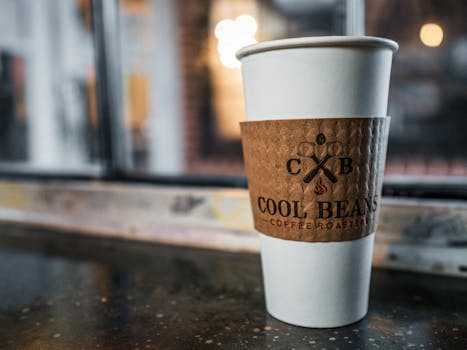 A branded coffee cup on a cafe table by a window, perfect for cozy coffee shop vibes.