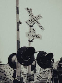 Artistic sepia-toned image of a railroad crossing sign and signal against a patterned backdrop.