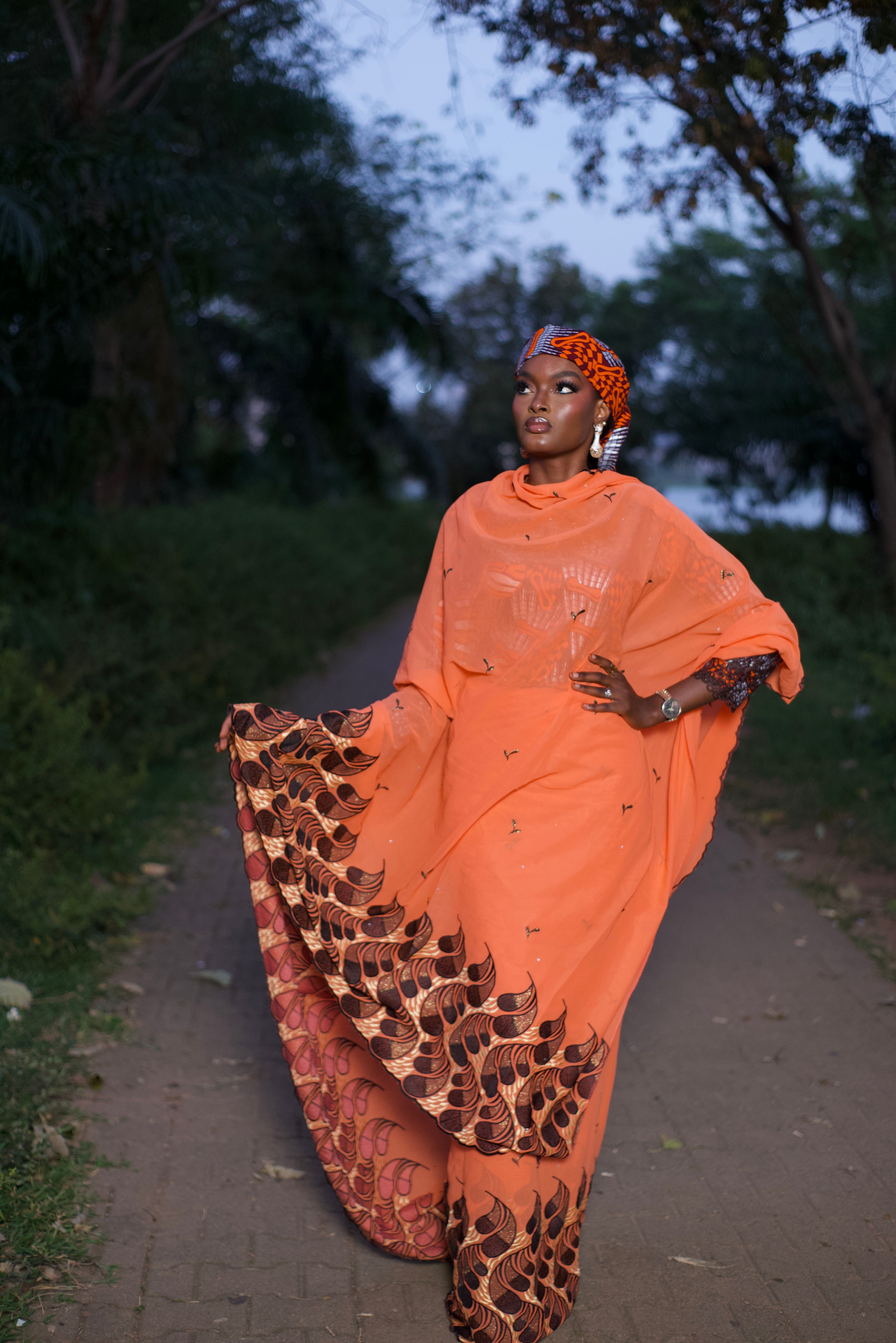 Portrait of a stylish woman in traditional Nigerian attire and headdress in a serene outdoor setting.
