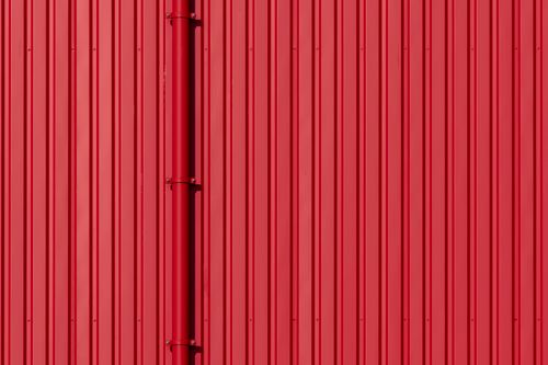 Free Vivid red corrugated metal wall with vertical drainpipe detail. Perfect for industrial and architectural themes. Stock Photo