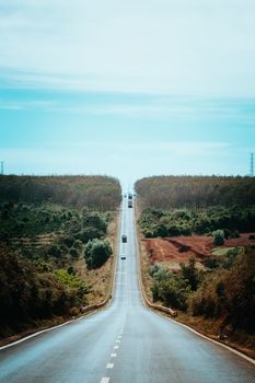 A long, straight road flanked by dense forest on a sunny day in Gia Lai, Vietnam.