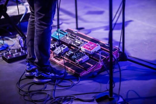 A musician performing with a pedalboard on a stage lit by blue lights. Vivid and dynamic.
