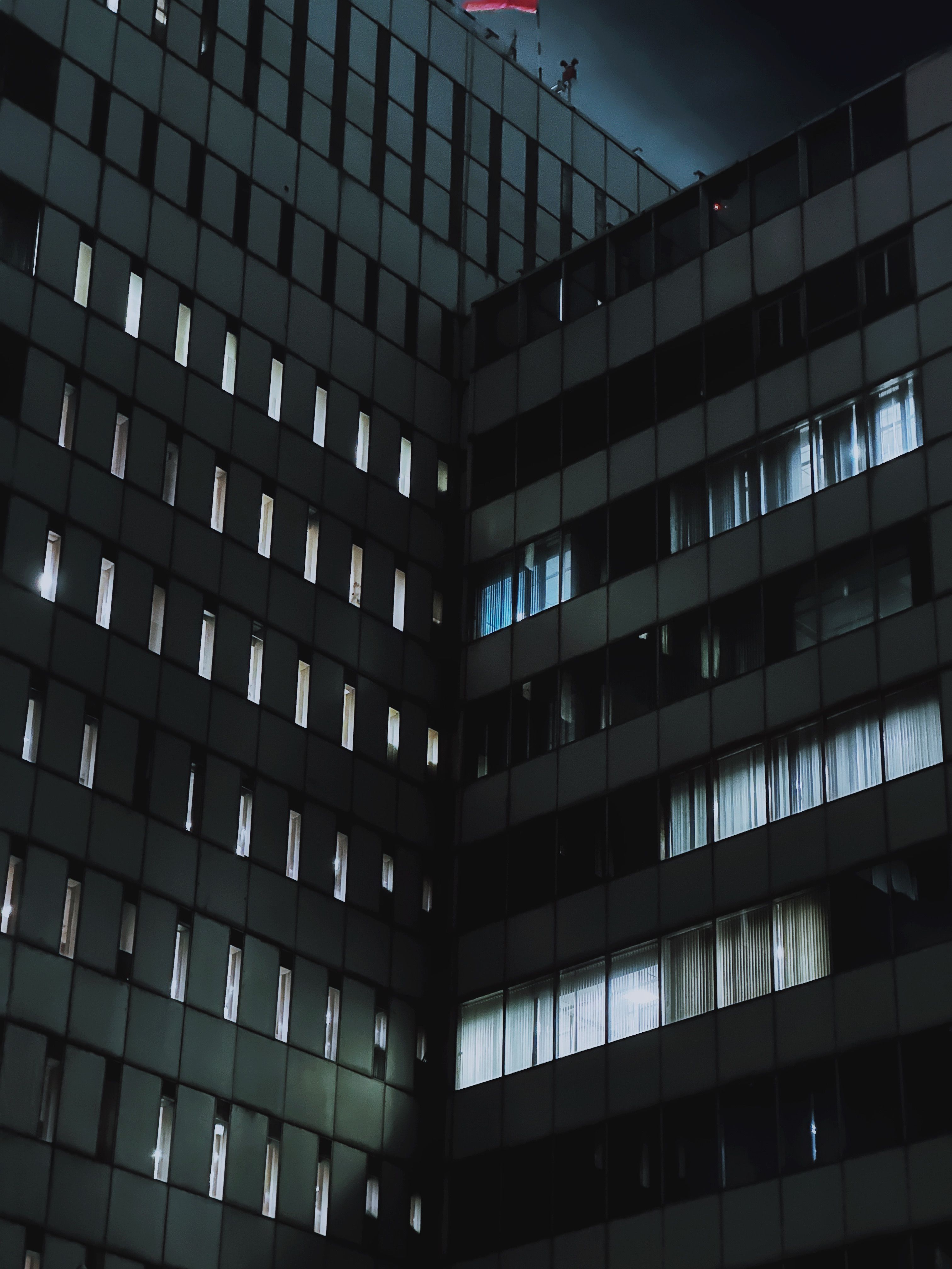 Dark moody architectural shot of urban buildings at night with lit windows.