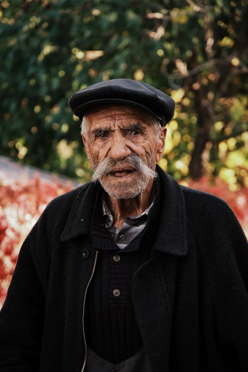 Free Portrait of an elderly man with a mustache wearing a hat and coat outdoors. Autumn colors. Stock Photo