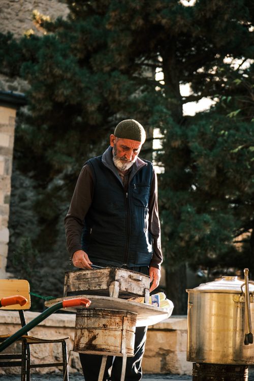Free An elderly man cooks traditional food outdoors, bathed in warm sunlight. Stock Photo