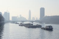 薄雾的天空下，一条平静的河面上，小船与朦胧的城市地平线相映成趣