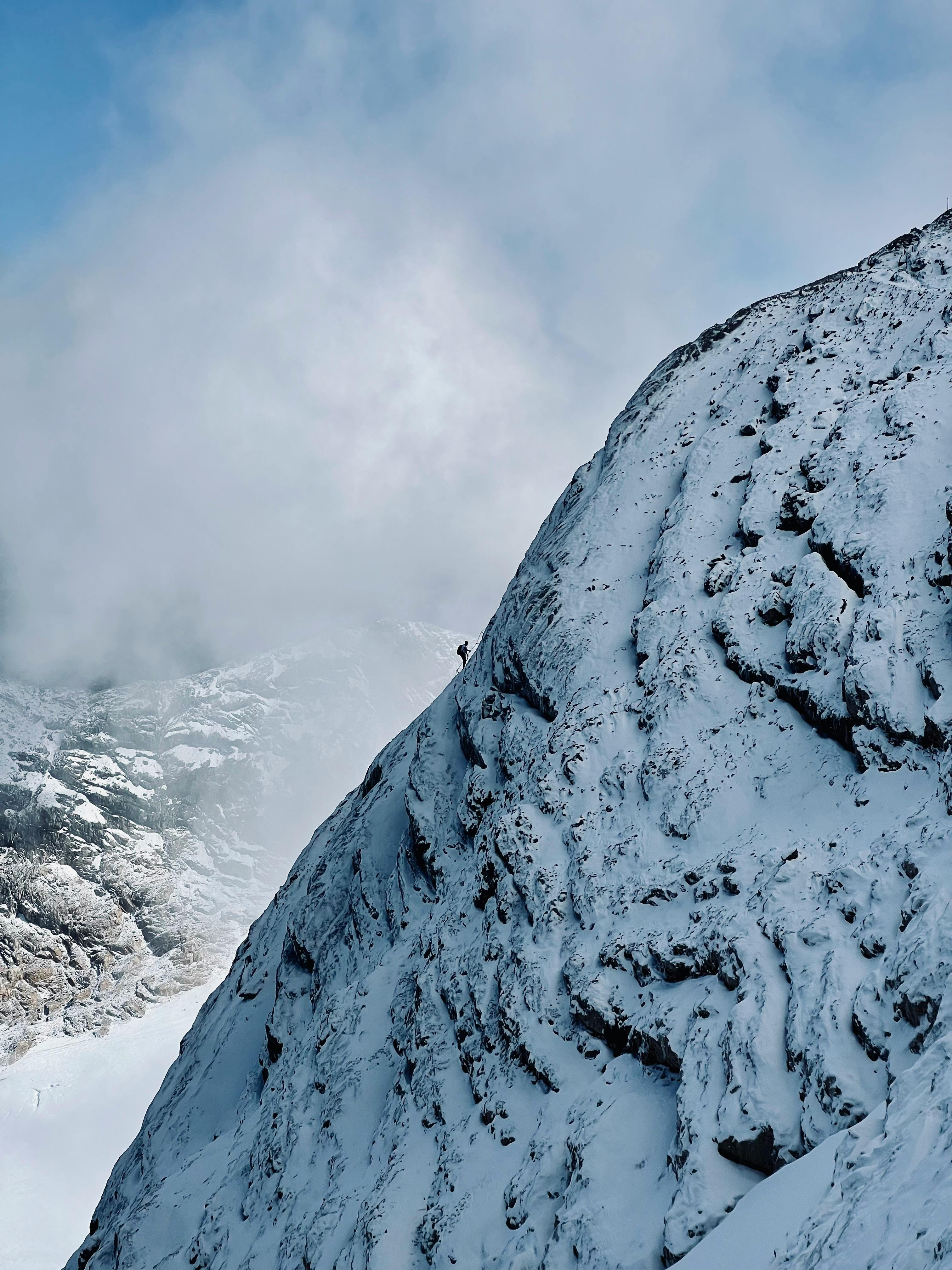 A solitary climber scales a snow-covered mountain peak in the Alps, showcasing extreme alpine adventure.