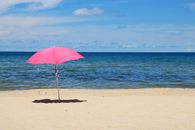 A vibrant pink umbrella on a serene beach with clear blue skies and ocean waves.