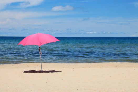 A vibrant pink umbrella on a serene beach with clear blue skies and ocean waves.