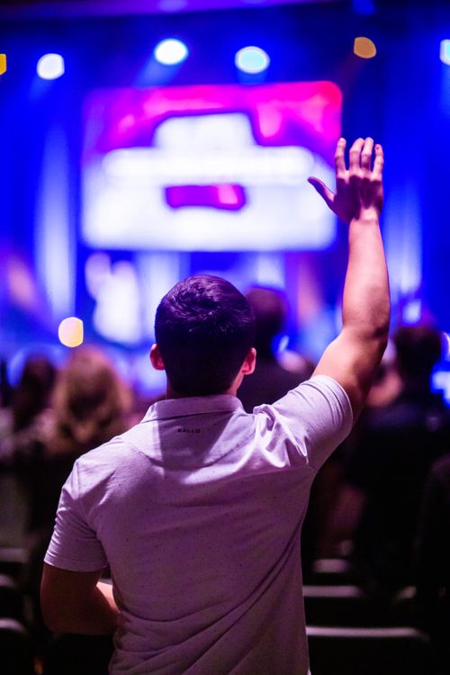 Free Back view of a man raising his hand at a concert with vibrant stage lights. Stock Photo