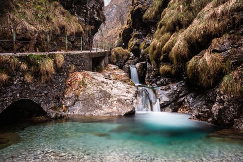 Free Peaceful waterfall with a rustic stone bridge in a rocky mountain landscape. Stock Photo