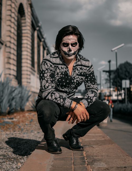 Free Young man with skeleton face paint crouching outdoors in urban environment. Stock Photo