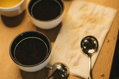 A warm coffee tasting setup with cups and spoons on a wooden table.