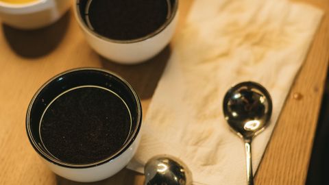A warm coffee tasting setup with cups and spoons on a wooden table.