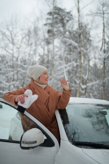 Smiling woman in warm clothes enjoying a snowy day outdoors by her car.